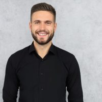 Happy,Brunette,Man,Is,Smiling,At,Camera,Isolated,Over,Gray Happy,Brunette,Man,Is,Smiling,At,Camera,Isolated,Over,Gray